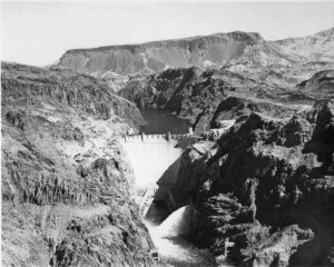 Black and white photograph of the valve houses discharging water from Arizona Canyon Wall of Hoover Dam in 1936.