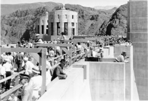 Black and white photograph of Boulder Dam dedication ceremony on September 30, 1935. The two intake towers are seen in the background while a crowd of people are gathered along the bridge and looking down the dam.