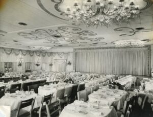 Black and white photo of The Opera House showing the long dining tables, the stage and ornate ceiling decor. s in 1947